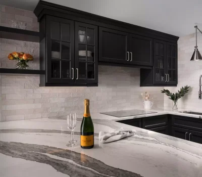Modern kitchen with black cabinets, marble countertops, champagne bottle, and a vase of orange flowers. Sleek faucet and neutral backsplash tiles.