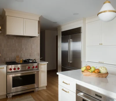Modern kitchen with stainless steel appliances, light cabinetry, and a fruit-filled wooden bowl. Elegant lighting and soft color palette create warmth.