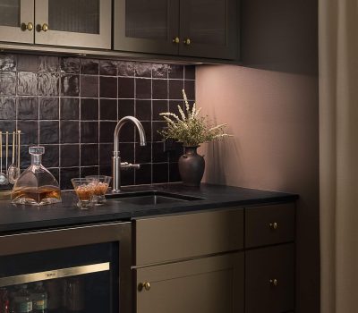 A cozy kitchen corner with dark cabinets, a black tiled backsplash, a sleek faucet, and a vase with flowers on the countertop.