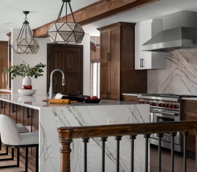 Modern kitchen interior featuring a marble island, wood cabinets, geometric pendant lights, and metal appliances, creating a sleek and inviting space.