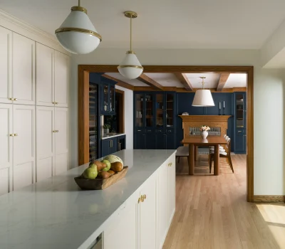 Modern kitchen with white cabinets, blue dining area, and wooden accents. Pendant lights, large windows, and a fruit bowl enhance the elegant design.