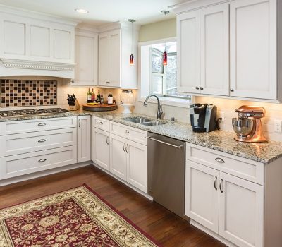 A modern kitchen with white cabinets, granite countertops, and stainless steel appliances. A patterned rug covers the wooden floor.