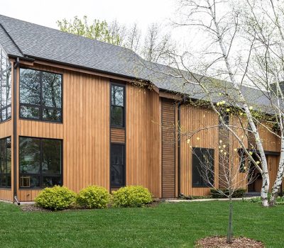 A modern wooden house with large windows surrounded by green lawn and trees, featuring a simple, sleek design.