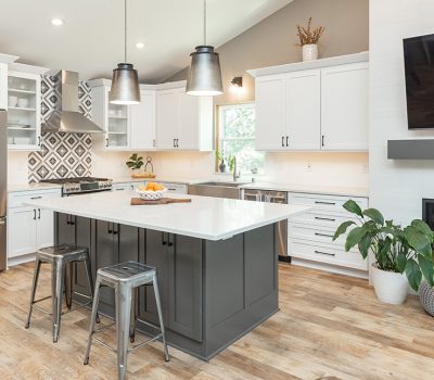 Modern kitchen featuring white cabinets, an island with stools, stainless steel appliances, and a decorative backsplash. A plant and fireplace add warmth.