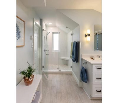 Modern bathroom with glass shower, white cabinets, and minimalist decor. Plants and neatly hung towels add a touch of color to the serene space.