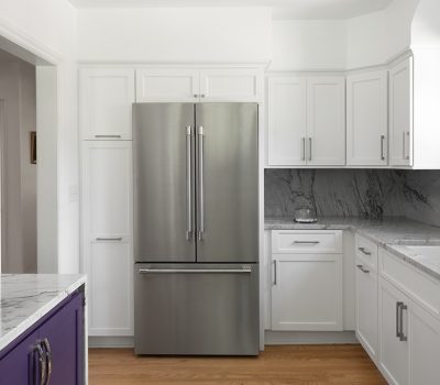 Modern kitchen with stainless steel refrigerator, white cabinets, and marble countertops. A purple cabinet with abstract art is displayed on the left.