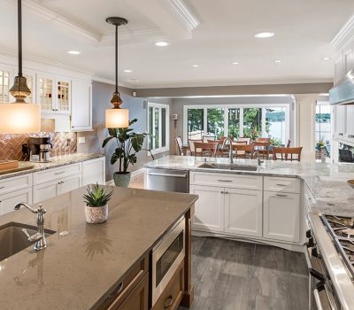 Spacious modern kitchen with large island, pendant lights, and view of dining area and lake. Bright, airy design with white cabinetry.