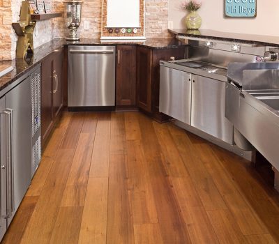 Modern kitchen with stainless steel appliances, stone backsplash, and wooden flooring. Shelves display decor items, and countertops hold kitchen essentials.