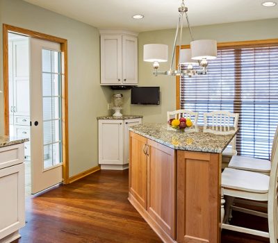 Modern kitchen featuring a granite island, wooden floors, pendant lighting, and white cabinets. Large window with blinds and a mixer on counter.