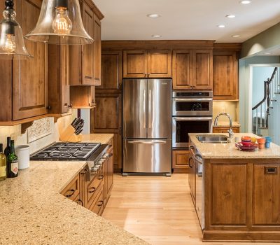 A modern kitchen features wooden cabinetry, granite countertops, stainless steel appliances, pendant lighting, and a vase of red flowers on the counter.