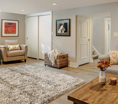 Cozy living room with modern decor, including a rug, armchairs, couch, and art on walls. Warm lighting creates an inviting atmosphere.