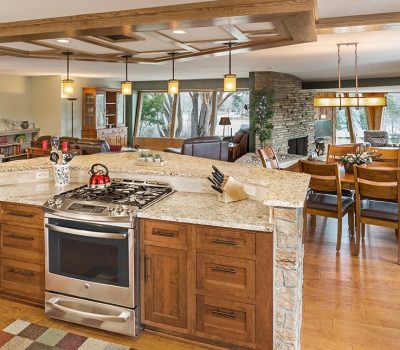Modern, open-concept kitchen with granite countertops, wooden cabinets, stainless steel appliances, and a cozy dining area overlooking large windows and a stone fireplace.
