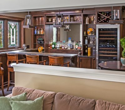 A cozy home bar with wooden furniture, stained glass windows, and a well-stocked shelf, featuring a Green Bay Packers helmet for decoration.