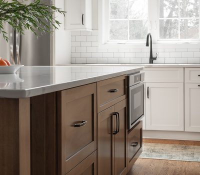 Modern kitchen with white cabinets, a dark wood island, and stainless steel appliances. A vase with branches and oranges decorates the countertop.