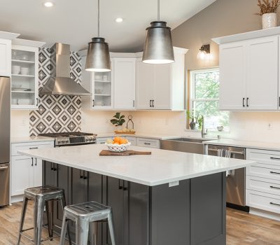 Modern kitchen with stainless steel appliances, white cabinets, and a patterned backsplash. Center island with pendant lights and bar stools. Bright, open space.