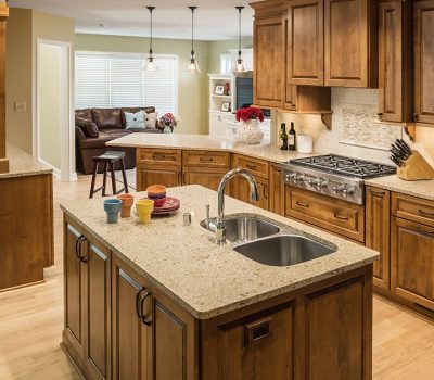 A spacious kitchen with wooden cabinets, dual sink, granite countertops, and stainless steel appliances. Open view to living area with leather sofa.