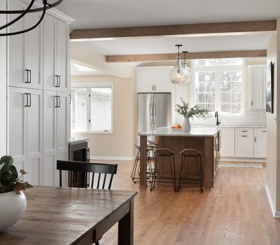 Spacious modern kitchen with white cabinets, wooden island, and dining area. Hardwood floors and staircase. Large window brings in natural light.