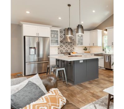 Modern kitchen with white cabinets, stainless steel fridge, geometric backsplash, and island with stools. Comfortable seating area with pillows in foreground.