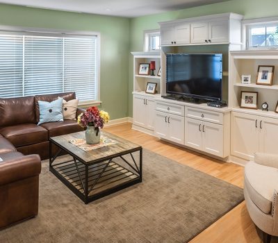 Cozy living room with a leather sectional sofa, beige armchair, entertainment center, large TV, coffee table with flowers, and decorative photo frames.