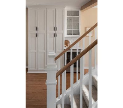 White stairway leads to a hallway with built-in cabinets, a glass-fronted cupboard, and wooden flooring. Warm, neutral wall colors complete the space.