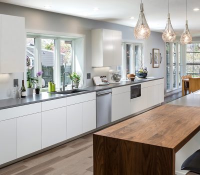 Modern kitchen with white cabinets, wooden island, pendant lights. Large windows overlook the garden. Includes dining table with chairs in the background.