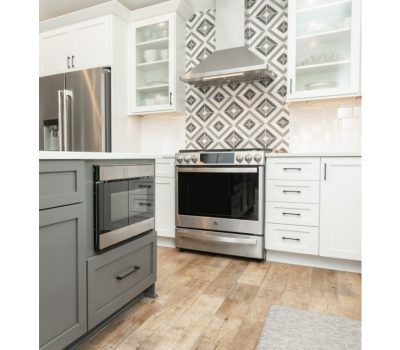 Modern kitchen with stainless steel fridge and oven, white cabinets, geometric tile backsplash, and wooden floor, creating a fresh, clean aesthetic.