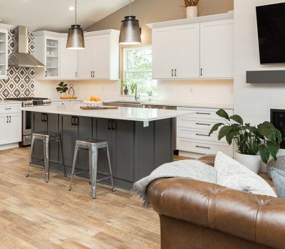 Modern kitchen with a center island, gray and white cabinets, stainless steel appliances, and a fireplace. Hardwood floors and a cozy sofa.