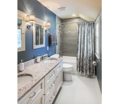 A modern bathroom features dual sinks on a granite countertop, a bathtub with a patterned curtain, and blue walls with stylish lighting fixtures.