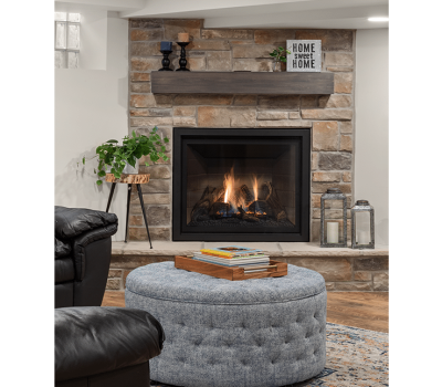 Cozy living room with a stone fireplace, round ottoman, leather chair, and decorative items on a shelf above the mantel.