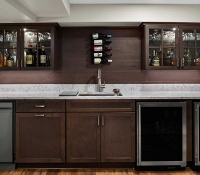 A modern home bar with marble countertop, dark wood cabinets, wine rack, glassware, and various bottles, creating a stylish beverage storage area.