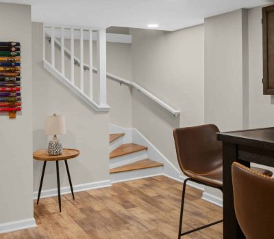 A cozy basement with wooden stairs, a small table lamp, and a collection of colorful bats mounted on the wall.
