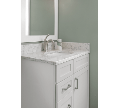 A bathroom vanity with a white marble countertop, faucet, and green wall. A large mirror reflects the room’s simple, elegant design.