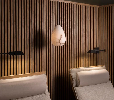 Wood-paneled room with pendant light and two loungers. Soft lighting creates a cozy atmosphere, ideal for relaxation. Vertical slats enhance modern aesthetics.