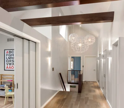 Bright hallway with wooden beams, modern lighting fixtures, and sliding doors. Child's room with alphabet poster visible on the left.