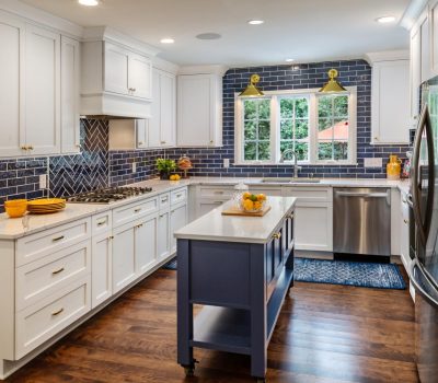 Bright kitchen with white cabinets, blue tile backsplash, and wooden floors. Features stainless steel appliances, a central island, and large window overlooking trees.