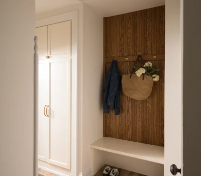 Cozy entryway with brick floor, wooden wall hooks holding a jacket and bag. White cabinets are visible, with shoes neatly arranged.