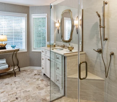 Elegant bathroom with a glass shower, marble tiles, and a vanity under a mirror. Natural light streams through the blinds, illuminating the space.