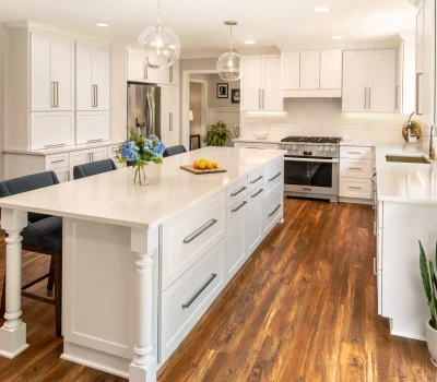 Modern kitchen with white cabinets, center island, stainless steel appliances, wooden floor, indoor plants, and pendant lights, creating a bright, inviting space.