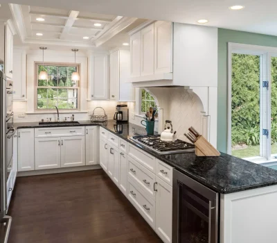 Modern kitchen with white cabinets, dark countertops, stainless steel appliances, and large windows providing a garden view. Natural light enhances the space.