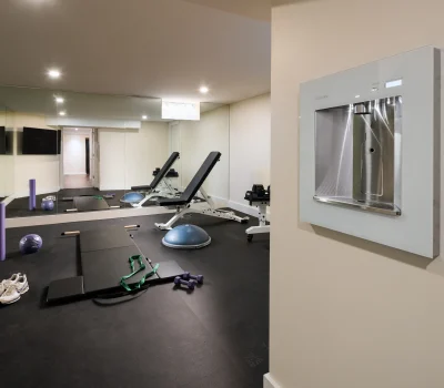 Home gym with a mirror, exercise equipment, water dispenser, and sneakers on the floor. Bright lighting reflects in the mirror.