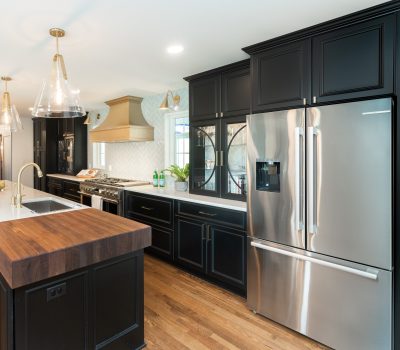 Modern kitchen with dark cabinets, stainless steel appliances, and wooden island. Elegant lighting fixtures hang above. Hardwood flooring completes the sleek design.