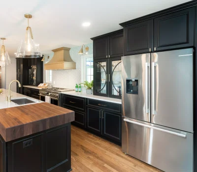 Modern kitchen with black cabinets, stainless steel appliances, and wood accents. Large island, elegant lighting, and plants complete the stylish design.