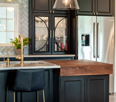 A modern kitchen with dark cabinets, stainless steel appliances, wooden countertop, brass fixtures, and a stylish pendant light above a sleek island.