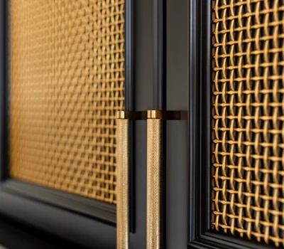 Close-up of a cabinet door with intricate cane weaving and elegant gold handles. The design features contrasting dark frame details.