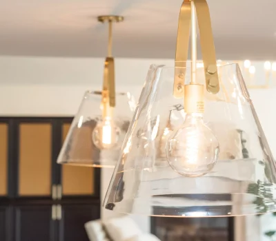 Close-up of modern pendant lights with clear glass shades, golden accents, and visible filament bulbs, illuminating a contemporary interior space with dark cabinets.
