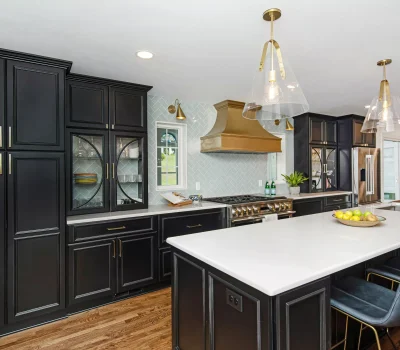 Modern kitchen with black cabinets, gold accents, large island, and elegant lighting. Bright and spacious, featuring hardwood floors and stainless steel appliances.