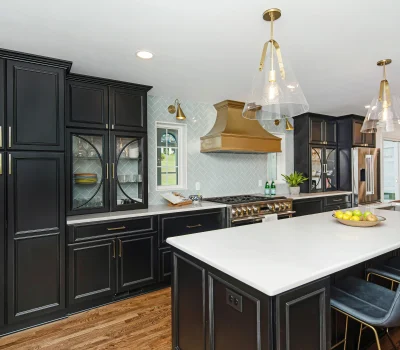 Modern kitchen with black cabinets, brass accents, white countertops, island with seating, pendant lights, and large stove. Contemporary design with wooden flooring.