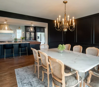 Elegant dining room with marble table, eight chairs, and chandelier. Adjacent modern kitchen features bar stools, pendant lights, and sleek black cabinets.