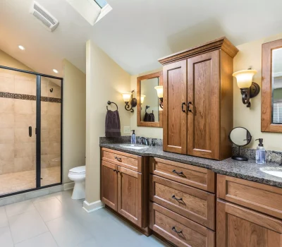 Modern bathroom with wooden cabinets, granite countertops, large shower with glass doors, and elegant lighting. Neutral tones create a warm, inviting atmosphere.