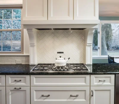 A modern kitchen featuring white cabinets, black granite countertops, a gas stove with a white kettle, and a window with a garden view.